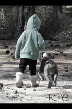 Blue and white American XL Bully puppy walking alongside a child in a hoodie and boots through a pine-covered forest, highlighting the breed’s adventurous and loyal temperament.